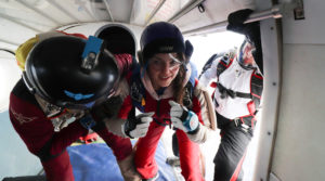 Une élève parachutiste prend position dans la porte de l'avion pour son premier saut autonome accompagnée de deux instructeurs.