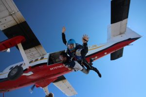 Un passager tandem débute sa chute libre en sautant d'un avion Twin Otter rouge et blanc.