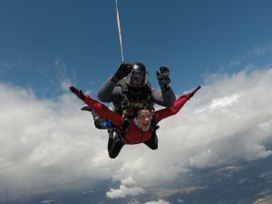 Une passagère tandem profite de sa chute libre, les bras ouverts, alors qu'elle passe a proximité d'une bande nuageuse.