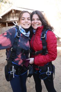 Une mère et sa fille portant des harnais de parachute sourient a la camera, joue contre joue.