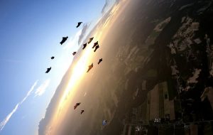 12 parachutistes vêtus de leur wingsuit volent en formation rapprochée au coucher du soleil.
