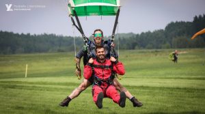 Une instructrice de parachute tandem atterri avec son passager en souriant au photographe.