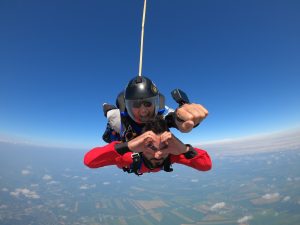 Saut en parachute tandem chez Parachute Voltige Un instructeur tandem sourit alors que son passager fait une forme de coeur avec ses mains.